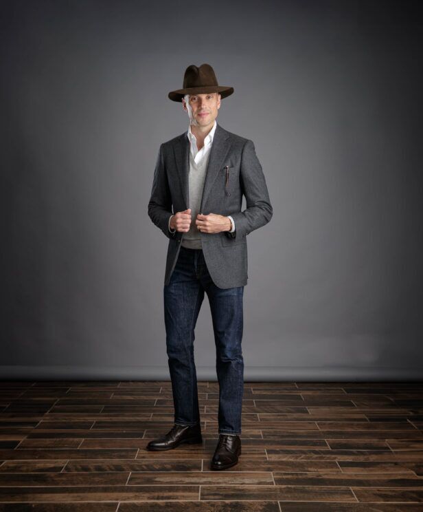 Charcoal flannel sport coat with grey V-neck sweater, white shirt and dark jeans, worn by a model in a brown fedora