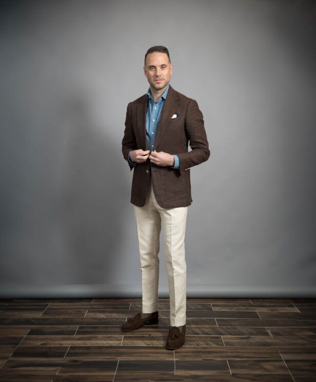 Chocolate brown linen sport coat with denim shirt, cream trousers and brown suede tassel loafers, worn by a model