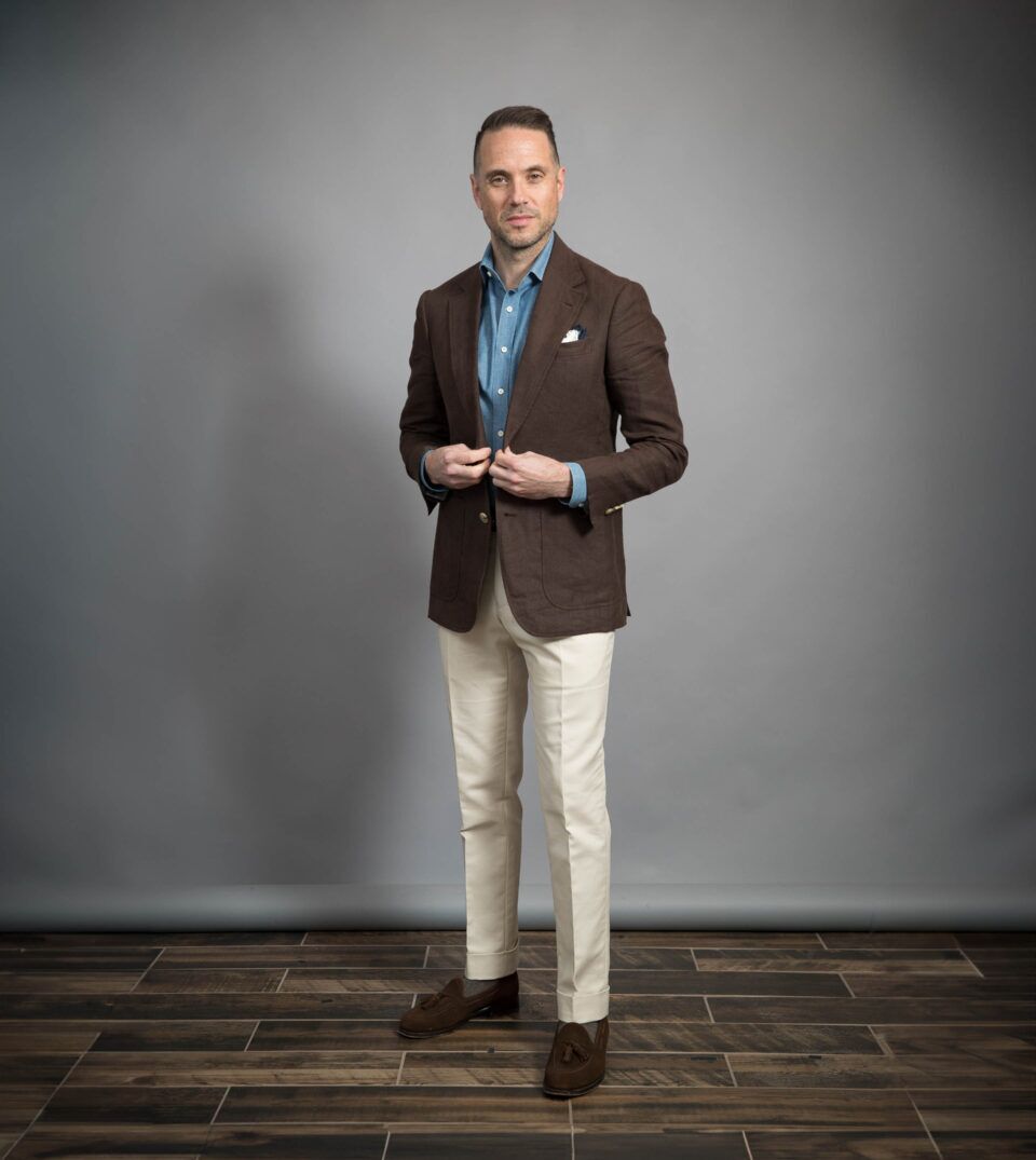 Chocolate brown linen sport coat with denim shirt, cream trousers and brown suede tassel loafers, worn by a model