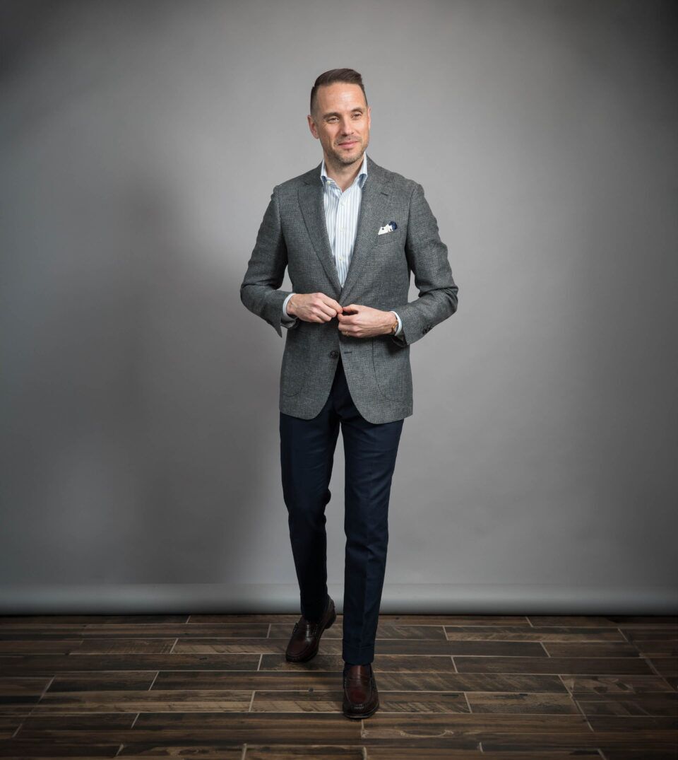 Grey puppytooth wool sport coat with blue striped shirt, navy trousers and brown loafers, worn by a model