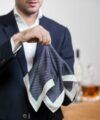 Navy houndstooth silk pocket square with cream border, held up by a model in a navy jacket