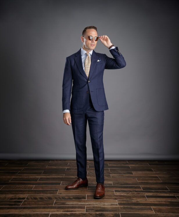 Navy hopsack suit with patch pockets, blue striped shirt and gold medallion tie, worn by a model