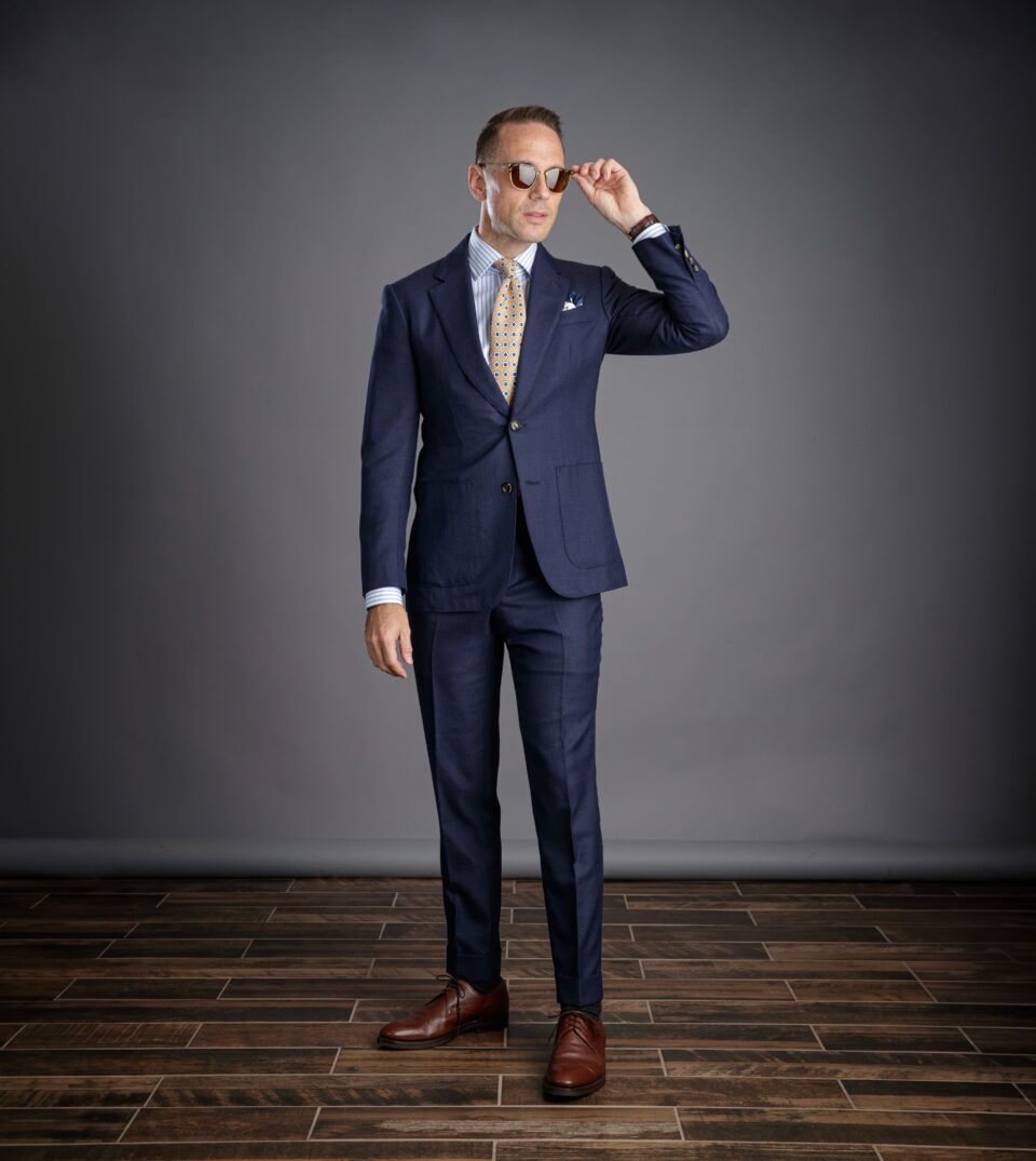 Navy hopsack suit with patch pockets, blue striped shirt and gold medallion tie, worn by a model