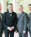 Black double-breasted peak lapel dinner jacket with bow tie, beside grey suits and ties, in a styled wedding scene