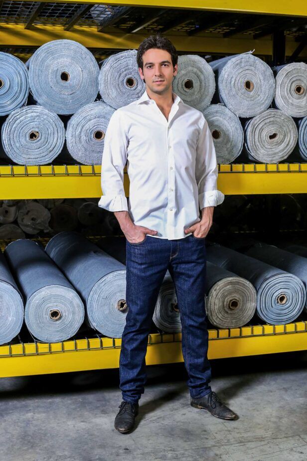 White cotton dress shirt with spread collar and rolled cuffs, worn with dark indigo jeans in a denim mill
