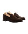 Dark brown suede penny loafers with leather soles, shown on cedar shoe trees in a product shot