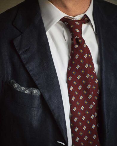 Burgundy silk necktie with blue and gold medallions, with white shirt and navy sport coat, worn by a model