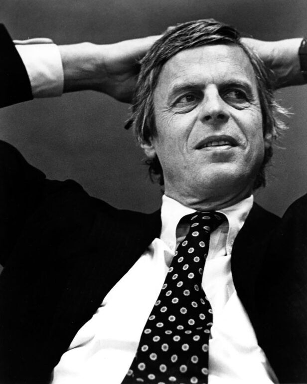 Dark silk necktie with white dot pattern, worn loosened with a white shirt and dark jacket by a man, black and white portrait