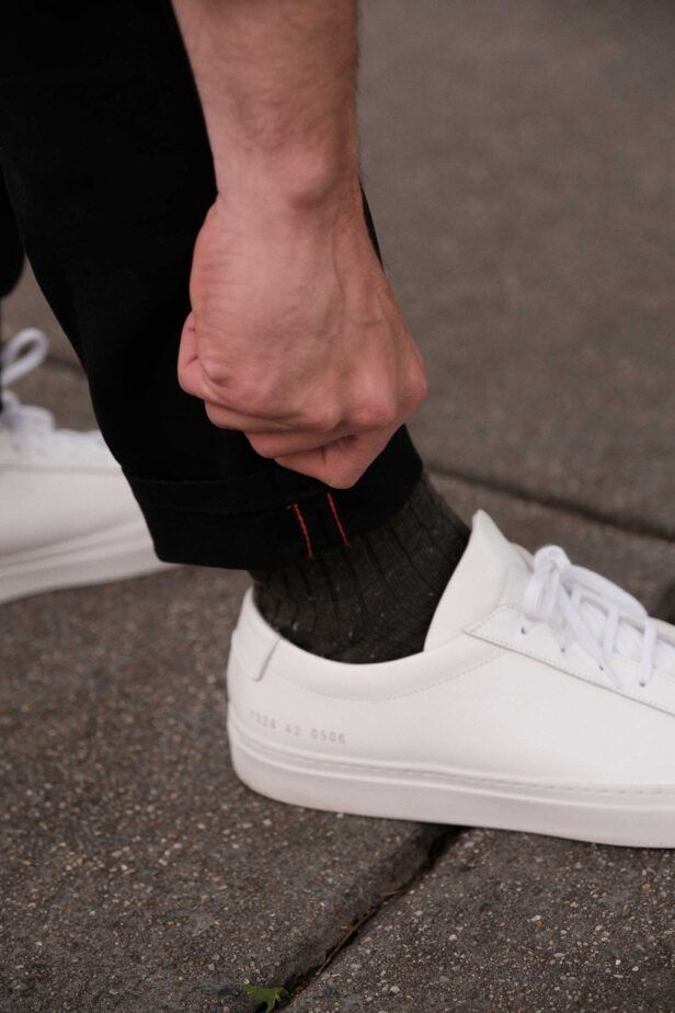 Black chinos with red accent stitching at the cuff, with olive socks and white sneakers, a close-up