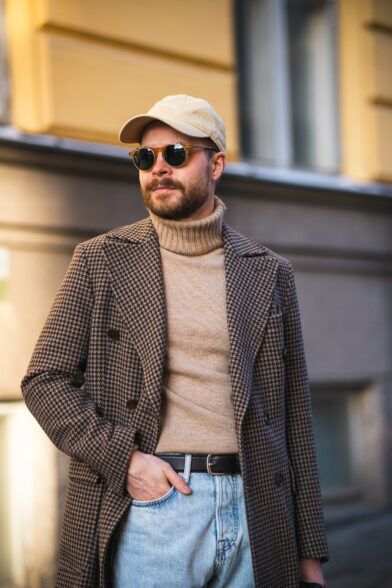 Brown houndstooth wool overcoat with camel turtleneck, light wash jeans and tan cap, worn by a model on a street