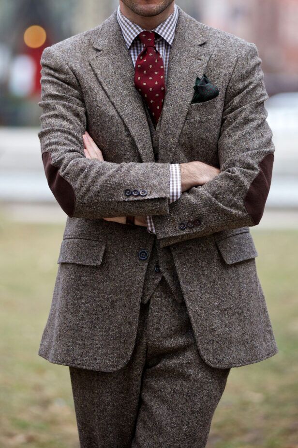 Brown donegal tweed three-piece suit with suede elbow patches, gingham shirt and burgundy pine cone tie, worn by a model