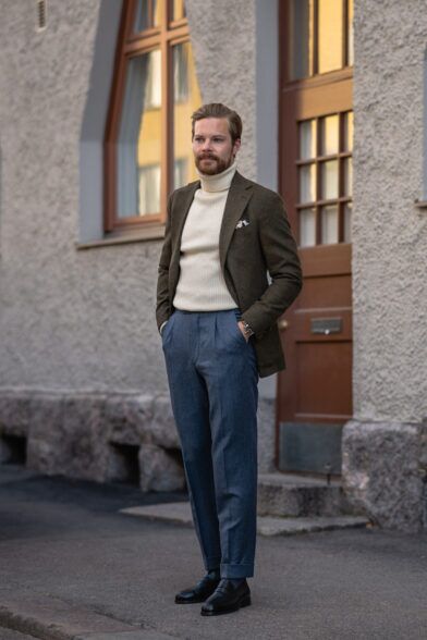 Olive green wool sport coat with cream ribbed turtleneck and blue flannel trousers, on a street