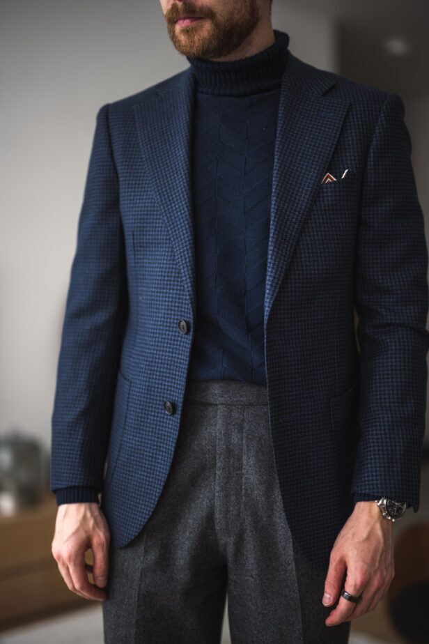 Navy houndstooth wool sport coat with navy cable-knit turtleneck and grey flannel trousers, worn by a model