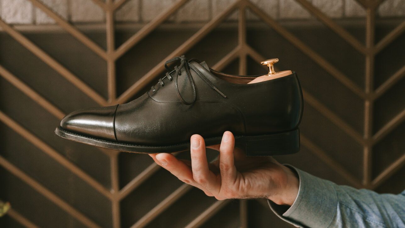 Black leather cap toe oxford with cedar shoe tree, held in a hand