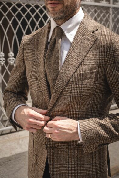 Brown glen plaid wool sport coat with matching tie and white shirt, worn by a model buttoning the jacket