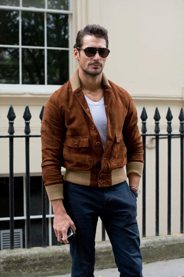 Tan suede bomber jacket with knit collar and cuffs, white t-shirt and navy chinos, worn by a model on a street