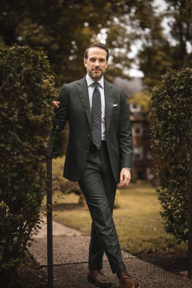 Forest green flannel suit with striped shirt, medallion silk tie and brown derbies, worn by a model in a garden