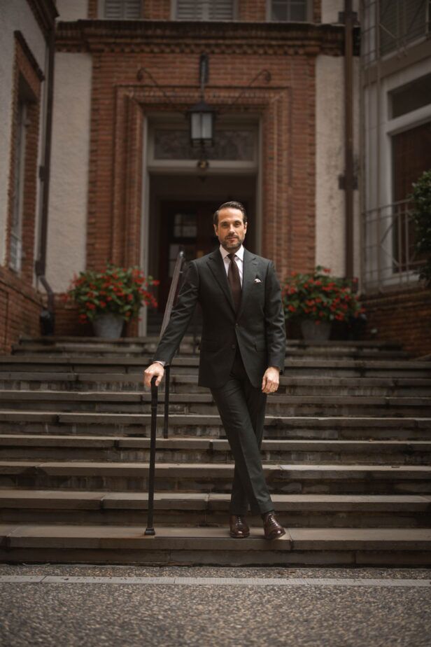 Forest green flannel suit with white shirt, brown tie and brown oxfords, worn by a model on brick building steps
