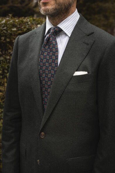 Forest green flannel suit with striped shirt, navy medallion tie and white pocket square, worn by a model