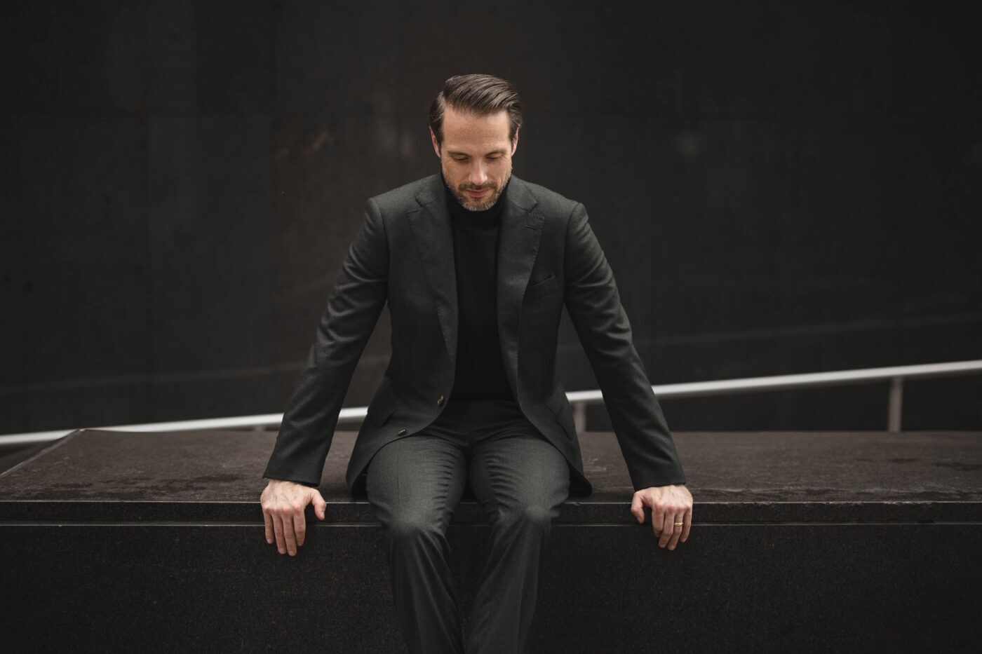 Dark forest green flannel suit with black turtleneck, worn by a seated model outdoors