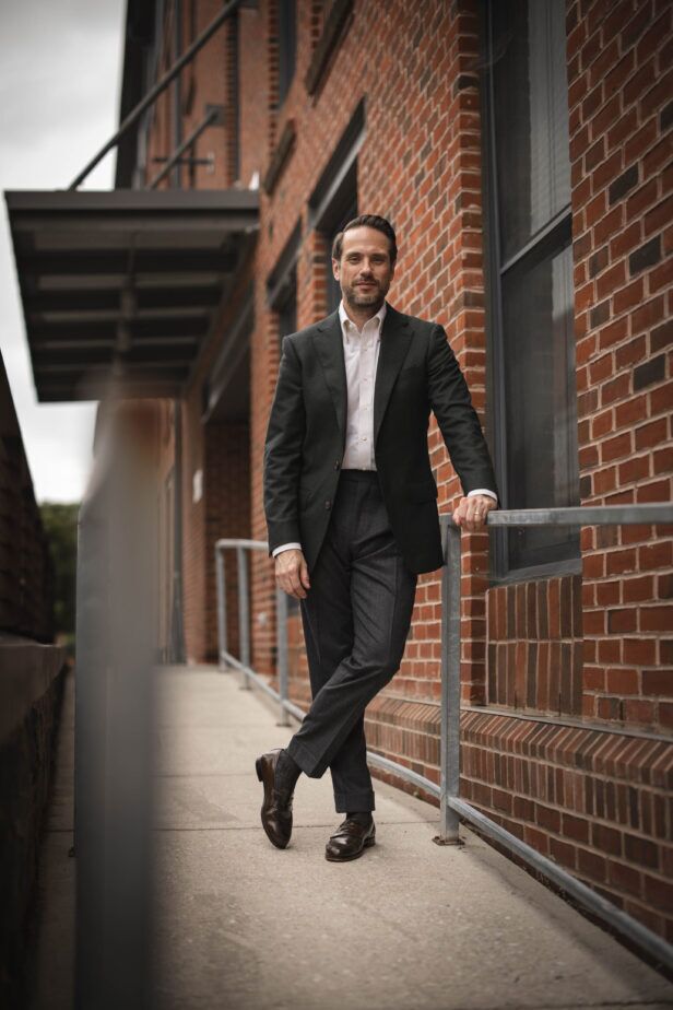 Dark green flannel sport coat with white shirt, charcoal trousers and brown penny loafers, worn by a model outdoors