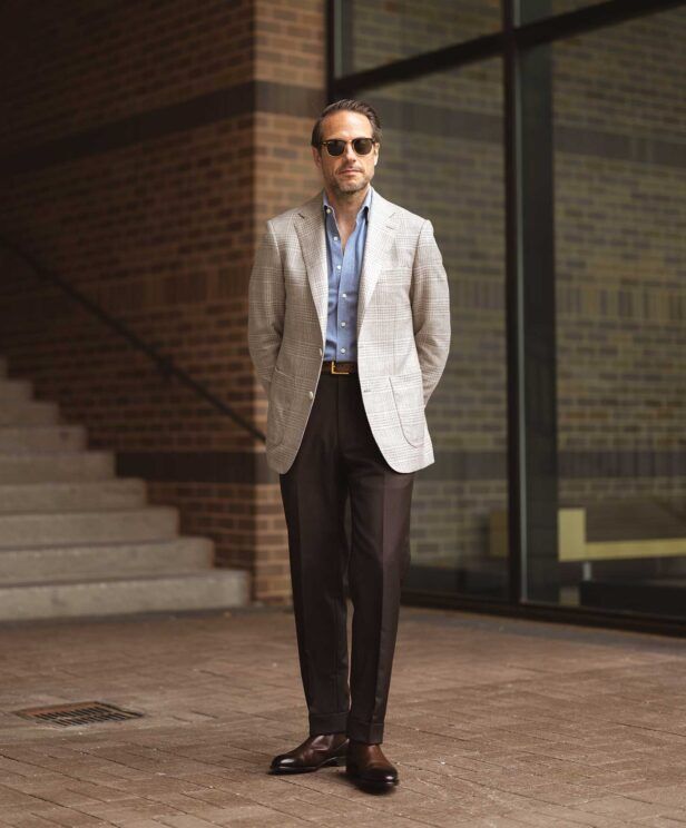 Light grey glen plaid sport coat with blue denim shirt, dark brown trousers and brown boots, worn by a model