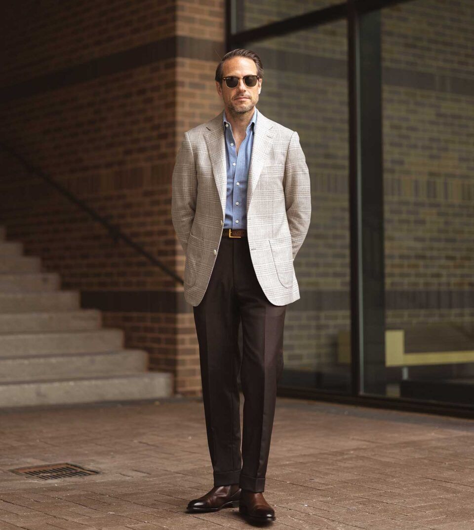Light grey glen plaid sport coat with blue denim shirt, dark brown trousers and brown boots, worn by a model