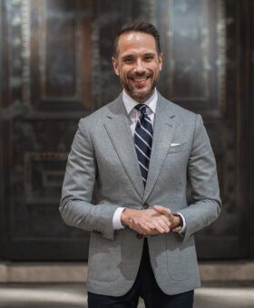 Light grey flannel sport coat with white shirt, navy striped tie and navy trousers, worn by a model