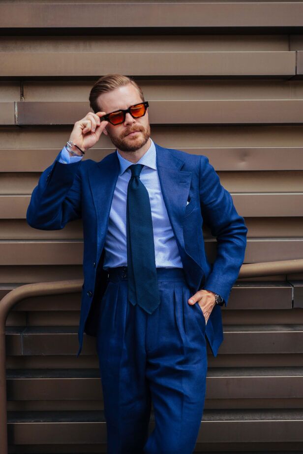 Bright blue linen suit with blue striped shirt, dark green grenadine tie and orange-tinted sunglasses, worn by a model