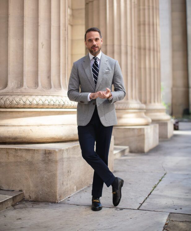 Light grey flannel sport coat with navy striped tie, white shirt and navy trousers, worn by a model outdoors