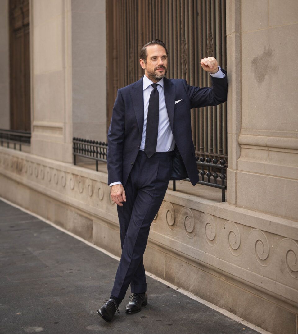 Navy flannel suit with light blue shirt, navy grenadine tie and black oxfords, worn by a model on a city street