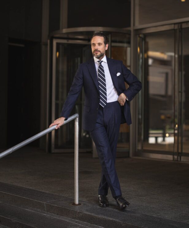 Navy flannel suit with striped shirt, navy striped tie and white pocket square, worn by a model outdoors