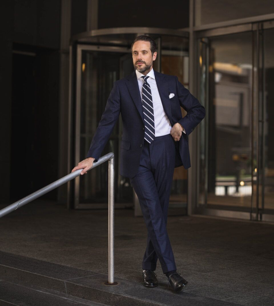 Navy flannel suit with striped shirt, navy striped tie and white pocket square, worn by a model outdoors
