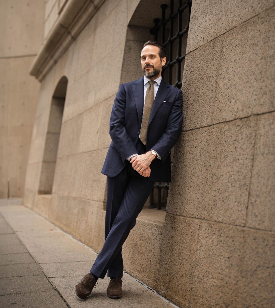 Navy flannel suit with striped shirt, brown tie and brown suede derbies, worn by a model on a city street