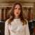 Ivory boat-neck long-sleeve dress in smooth satin, worn by a woman in a warmly lit interior