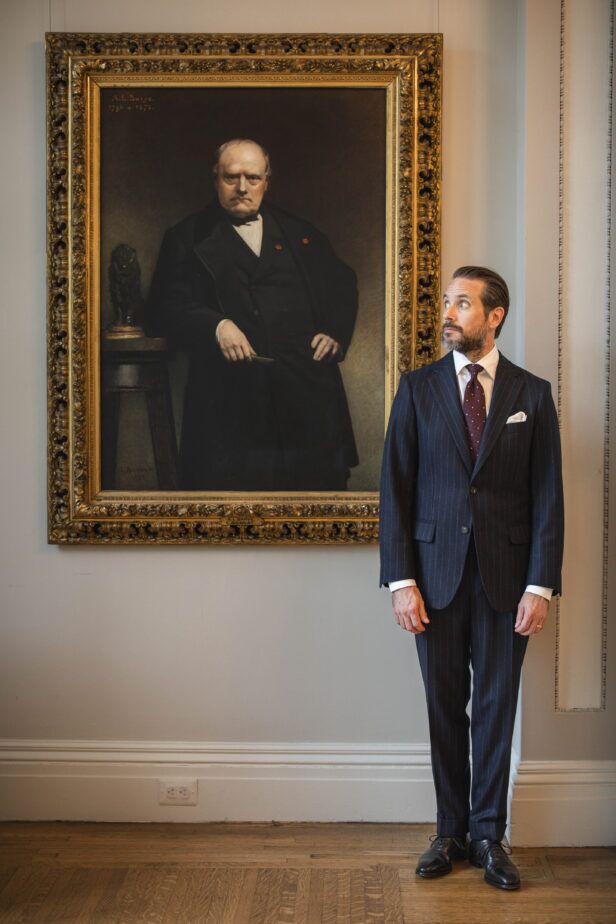 Navy chalk stripe suit with burgundy dotted tie and white pocket square, beside a framed portrait