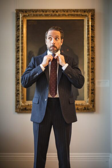 Navy chalk stripe flannel suit with white shirt and burgundy dotted silk tie, worn by a model in a gallery