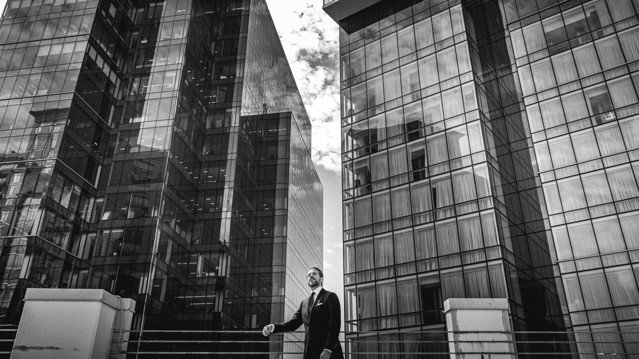 Pinstripe suit with white shirt and tie, worn by a model among glass towers in a black and white street scene