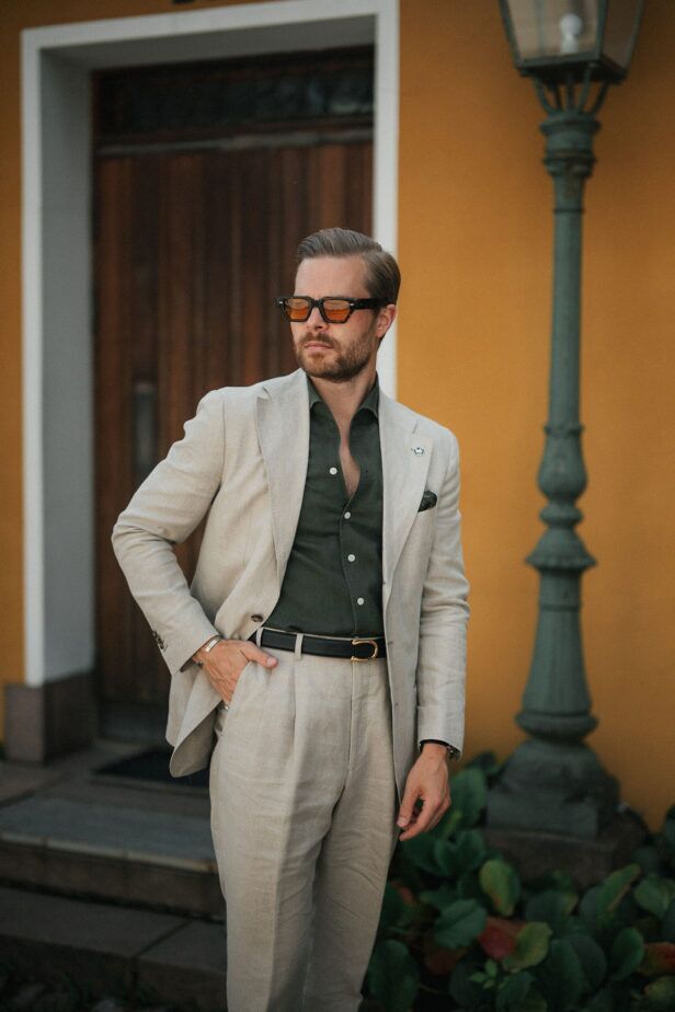 Cream linen suit with olive green shirt, black belt and amber-tinted sunglasses, worn by a model in a styled street scene