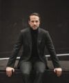 Forest green flannel suit with black turtleneck, worn by a model seated on a stone ledge