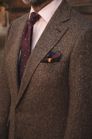 Brown donegal tweed suit jacket with pink shirt, burgundy dotted tie and printed pocket square, close-up on a model