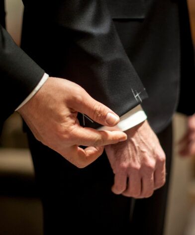 Black tuxedo jacket sleeve with white shirt cuff and hand-stitched basting mark, a close-up detail