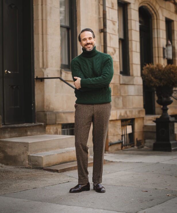 Brown donegal tweed trousers with cuffs, worn with a green cable-knit turtleneck and brown loafers on a city street