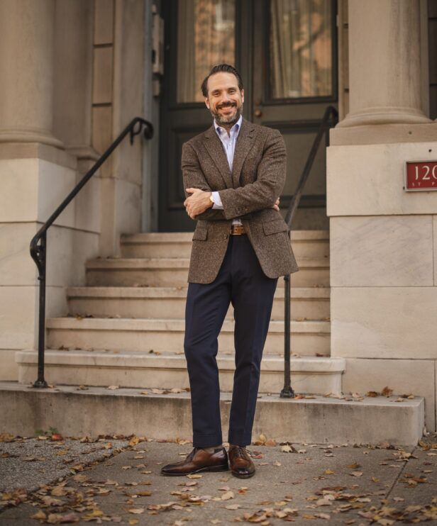 Brown donegal tweed sport coat with blue shirt, navy trousers and brown derbies, worn by a model on steps