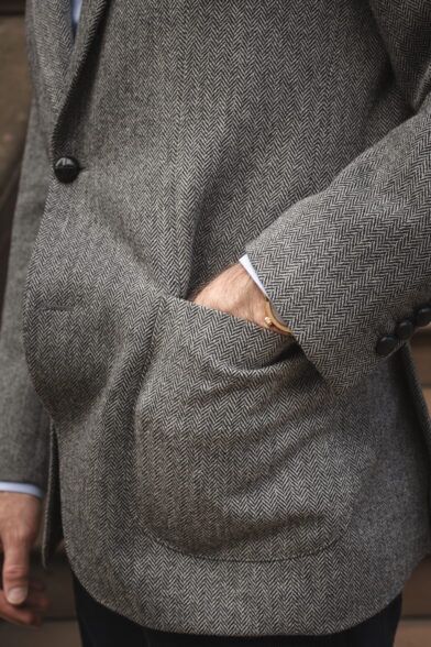 Grey herringbone tweed sport coat with patch pocket and dark buttons, a close-up detail on a model