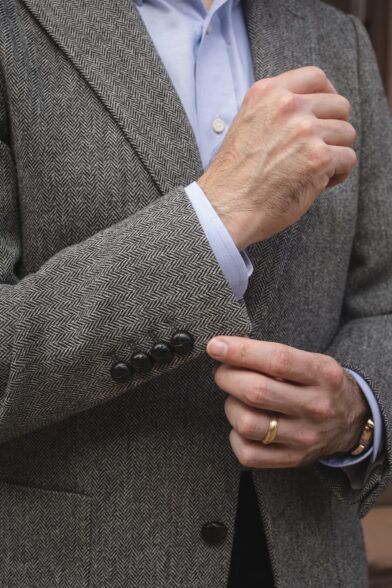 Grey herringbone tweed sport coat with dark leather buttons and blue shirt cuff, a close-up of the sleeve