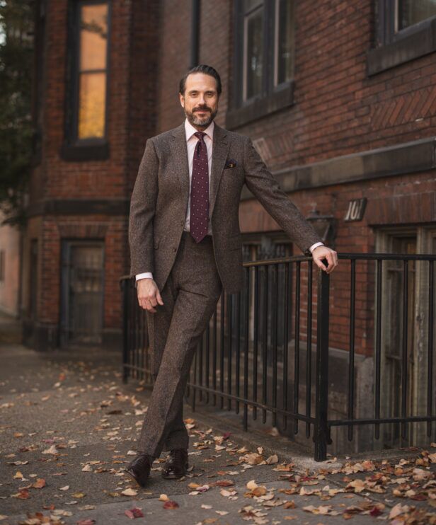 Brown donegal tweed suit with pink shirt, burgundy dotted tie and brown oxfords, worn by a model on a city sidewalk