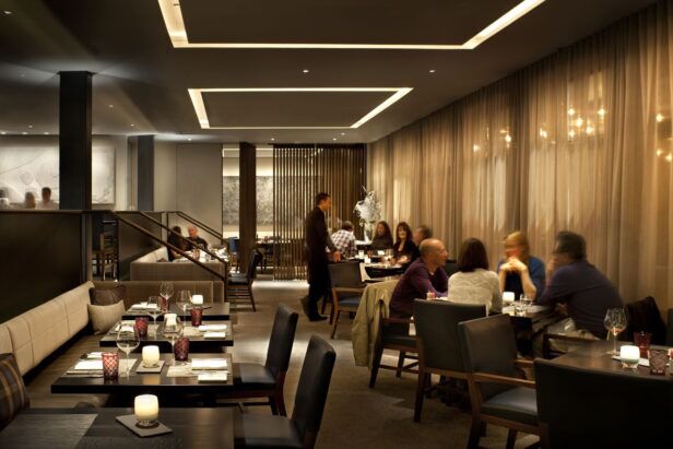 Dimly lit hotel restaurant dining room with set tables, candles and diners, a styled lifestyle scene