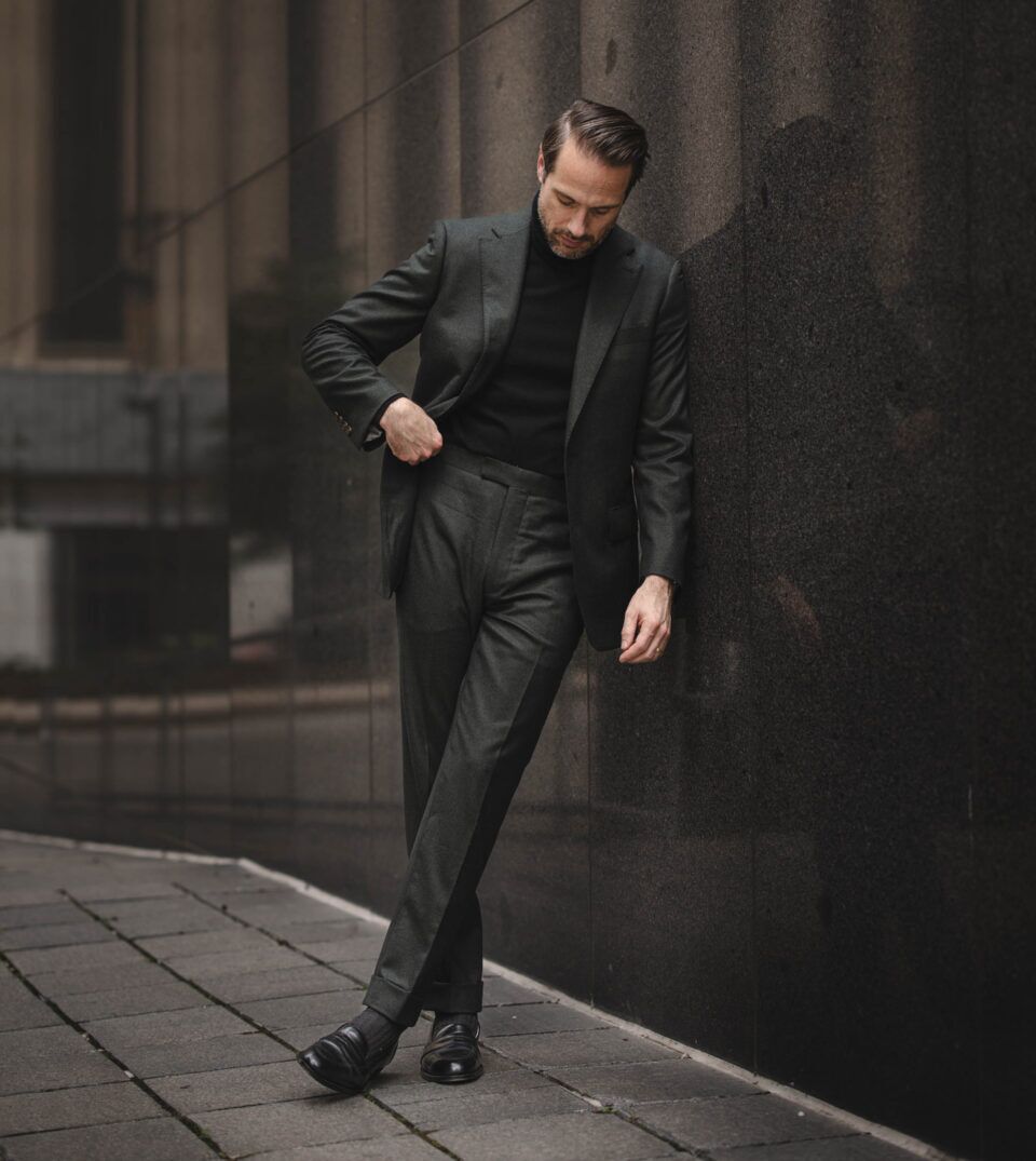 Dark forest green flannel suit with black turtleneck and black loafers, worn by a model on a city street