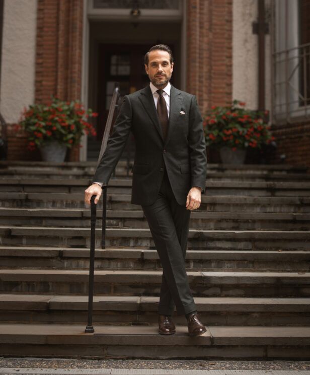 Dark green flannel two-button suit with white shirt, brown knit tie and brown oxfords, worn by a model on steps